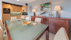 A modern kitchen with wooden cabinets, a microwave, and a dining area with a glass table and chairs. - Goldsands II 302 with parking by Interhome (De Haan)