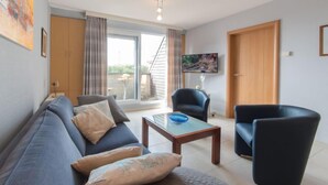A modern living room with a sofa, armchairs, a coffee table, and a TV mounted on the wall. - Goldsands II 302 with parking by Interhome (De Haan)
