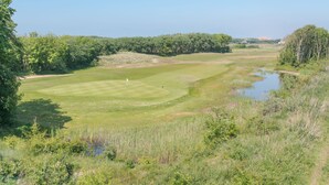A golf course with a pond, surrounded by dense trees and greenery. - Goldsands II 302 with parking by Interhome (De Haan)