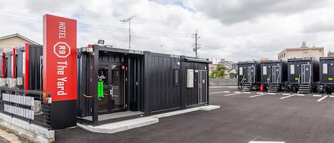 Un hotel con un letrero rojo que dice "HOTEL The Yard" y un edificio negro con habitaciones numeradas.