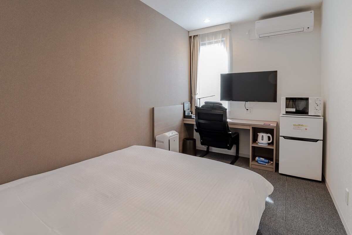 Une chambre d’hôtel équipée d’un lit, d’un bureau avec une chaise, d’une télévision, d’un four à micro-ondes et d’un réfrigérateur.