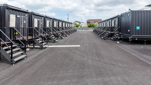 A row of identical modular units with external stairs, arranged in a linear fashion on a paved surface. - HOTEL R9 The Yard Buzen (Buzen)