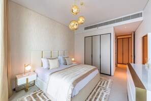 A modern bedroom with a large bed, bedside lamps, a wardrobe, and a vanity with a mirror.