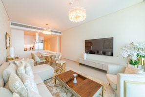 A modern living room with a sofa set, a coffee table, a chandelier, and a dining area in the background.