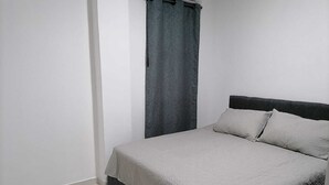 A bedroom with a bed, a dark headboard, and a grey curtain.