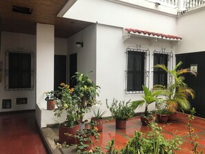 Un patio con macetas, suelo de baldosas y un edificio blanco con marcos de ventanas negros.