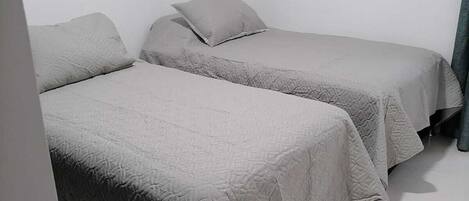 Een kamer met twee bedden, elk met een grijze spreidek en kussens.