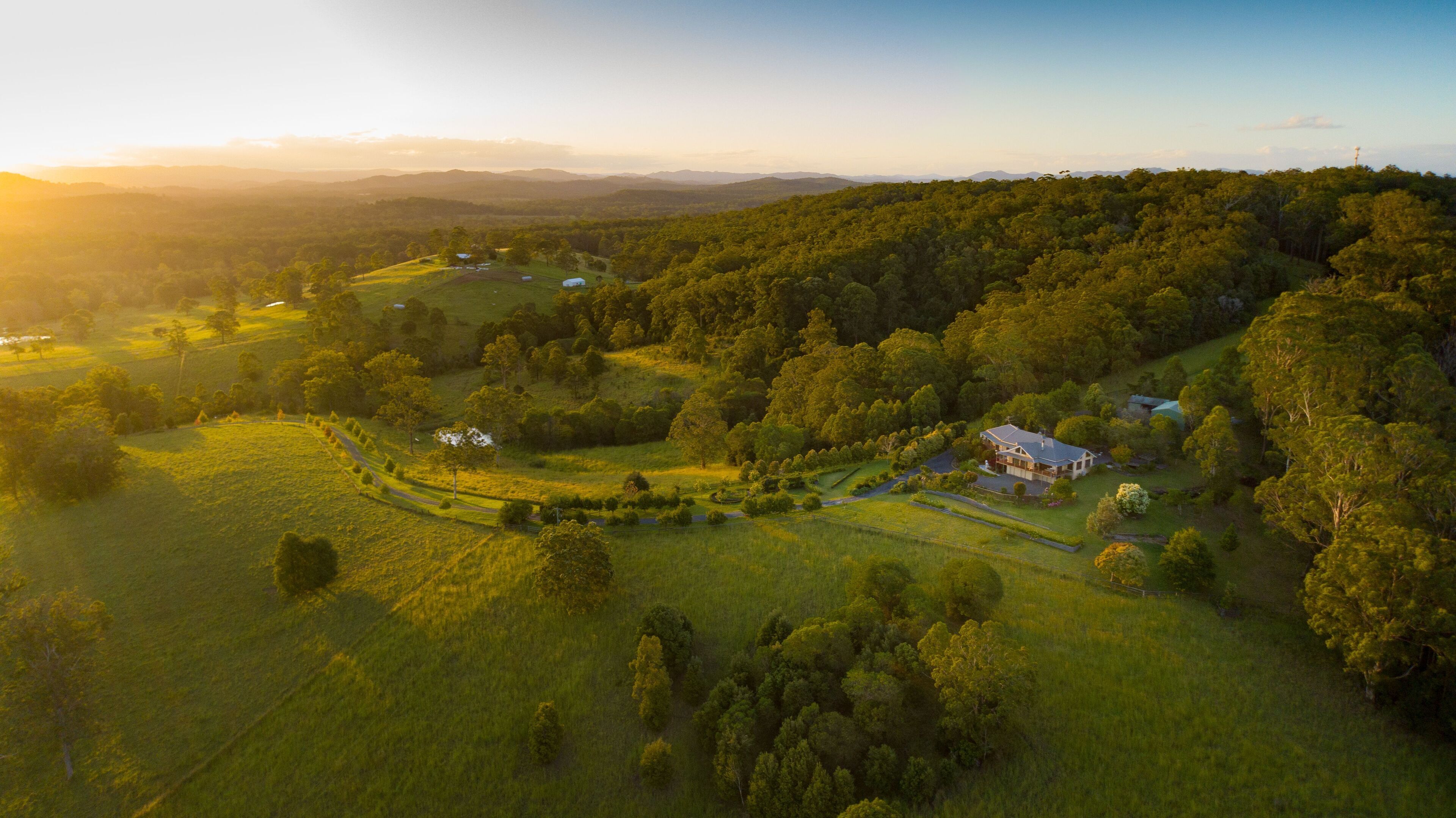 Vista aérea de una propiedad rural con colinas ondulantes, densos bosques y una casa grande rodeada de campos abiertos.