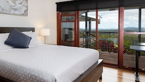 Een slaapkamer met een groot bed, een nachtkastje, een lamp en een balkon met uitzicht op het landschap.