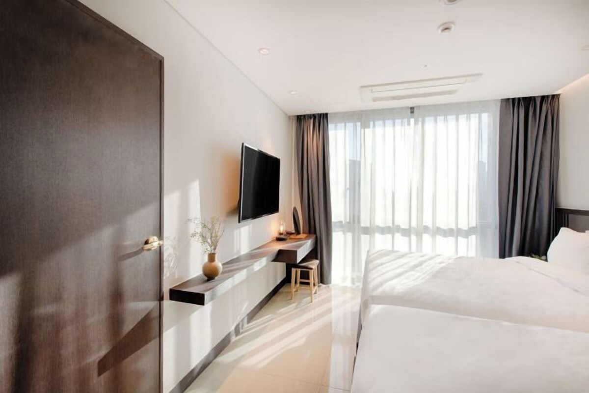 A hotel room with a bed, a desk, a TV, and a large window with curtains.