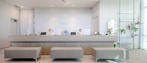 A modern reception desk with three grey benches, a laptop, and a sign reading "UNIVERSITET".