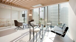 A modern office space with glass partitions, a variety of seating including a sofa and chairs, and a ceiling with wooden slats.