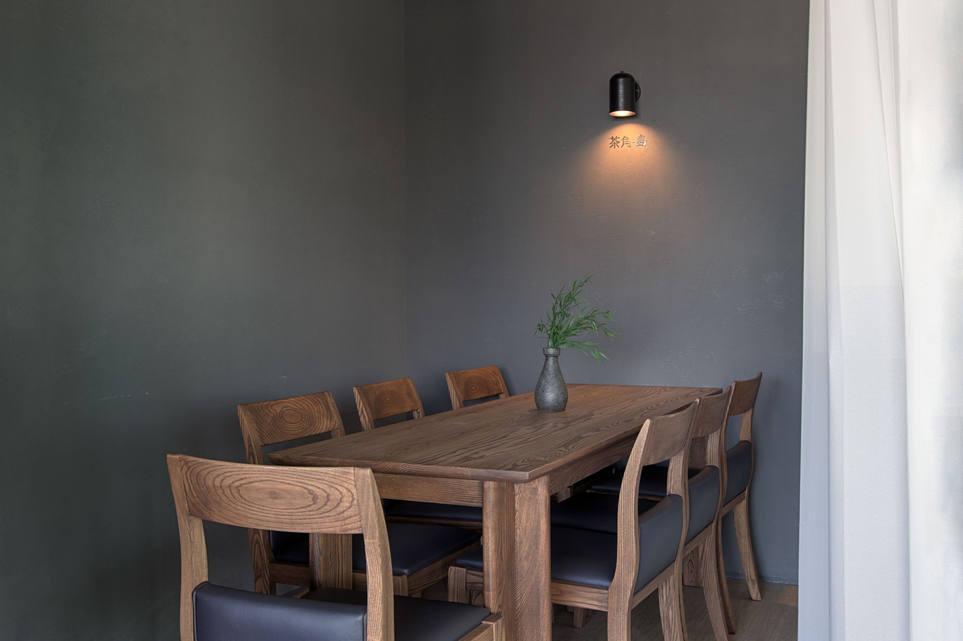 Una mesa de comedor de madera con seis sillas, un florero con una planta y una lámpara fijada a la pared.