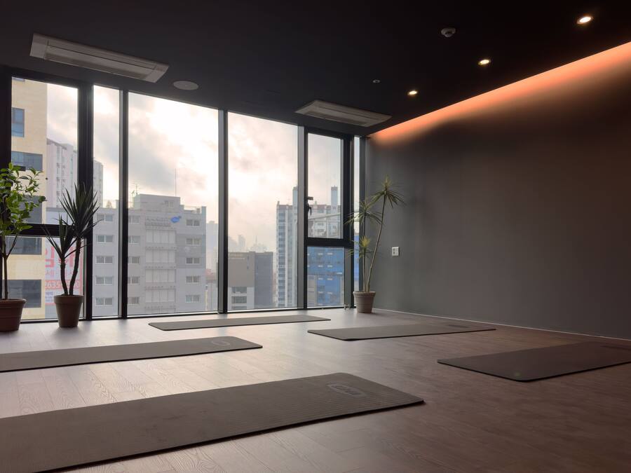 A spacious room with large windows, wooden flooring, and several yoga mats.