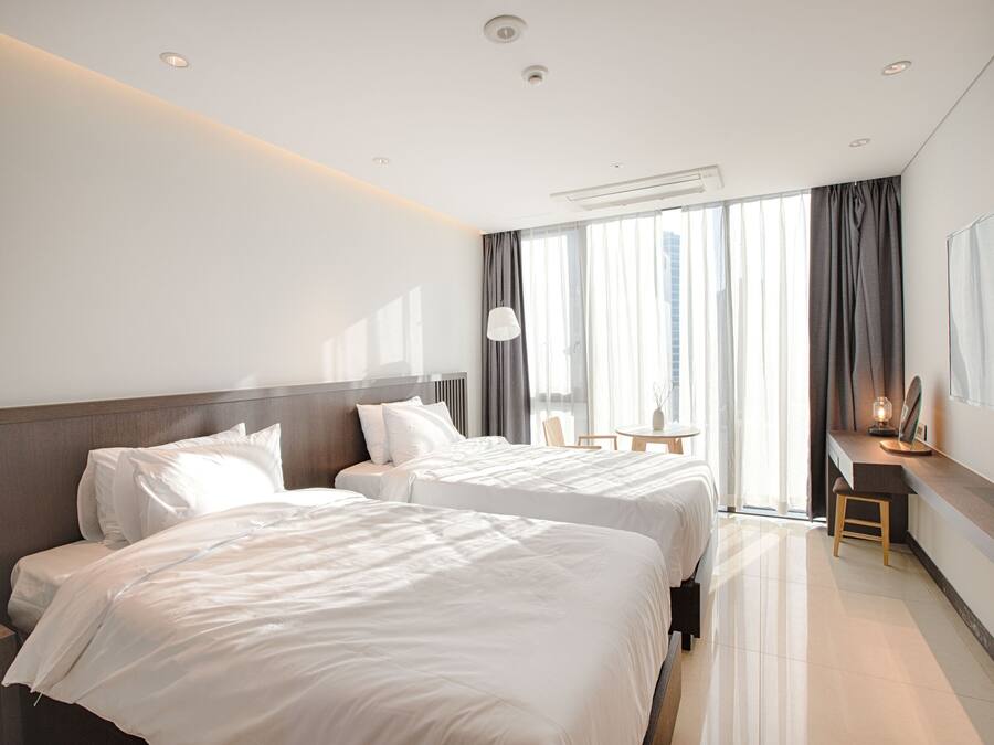 A hotel room with two beds, a desk, a chair, and a large window with curtains.