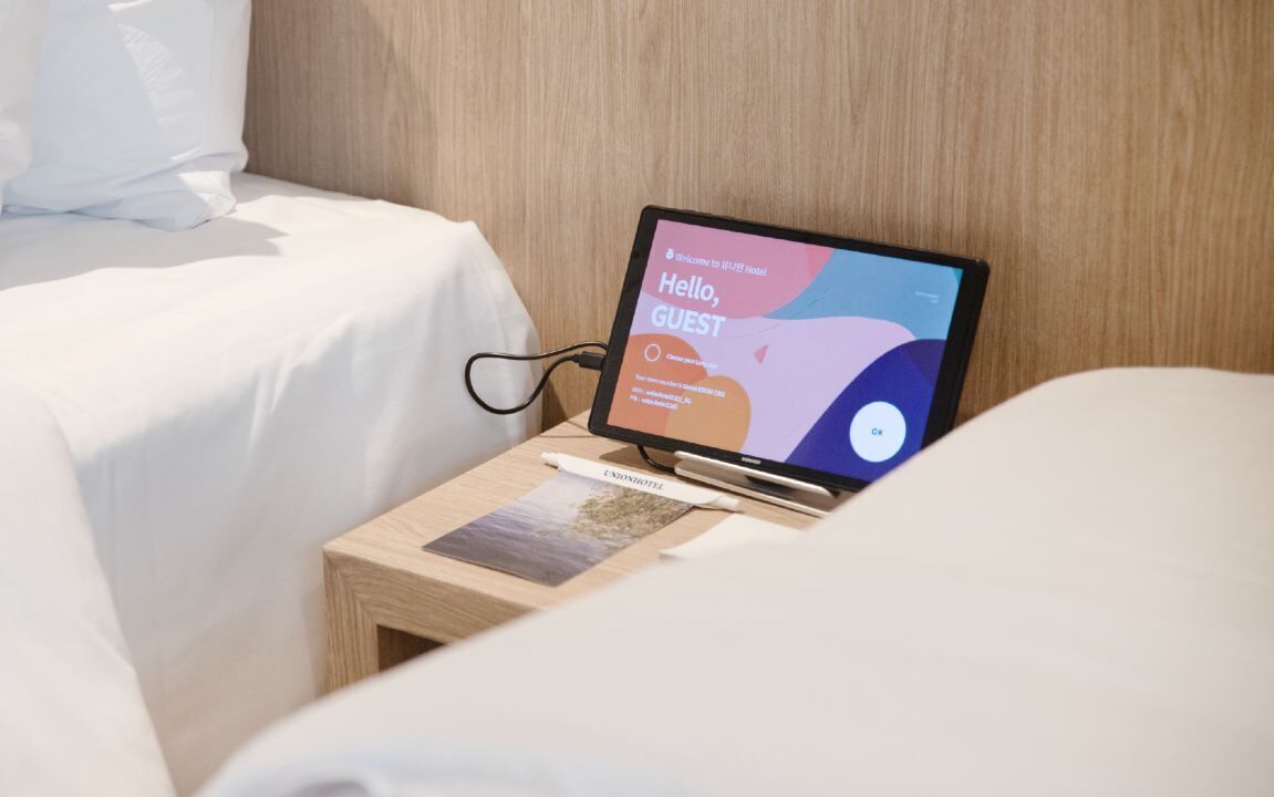 Un ordinateur portable est posé sur une table de chevet, et l’écran affiche le message : « Bonjour, invité ».