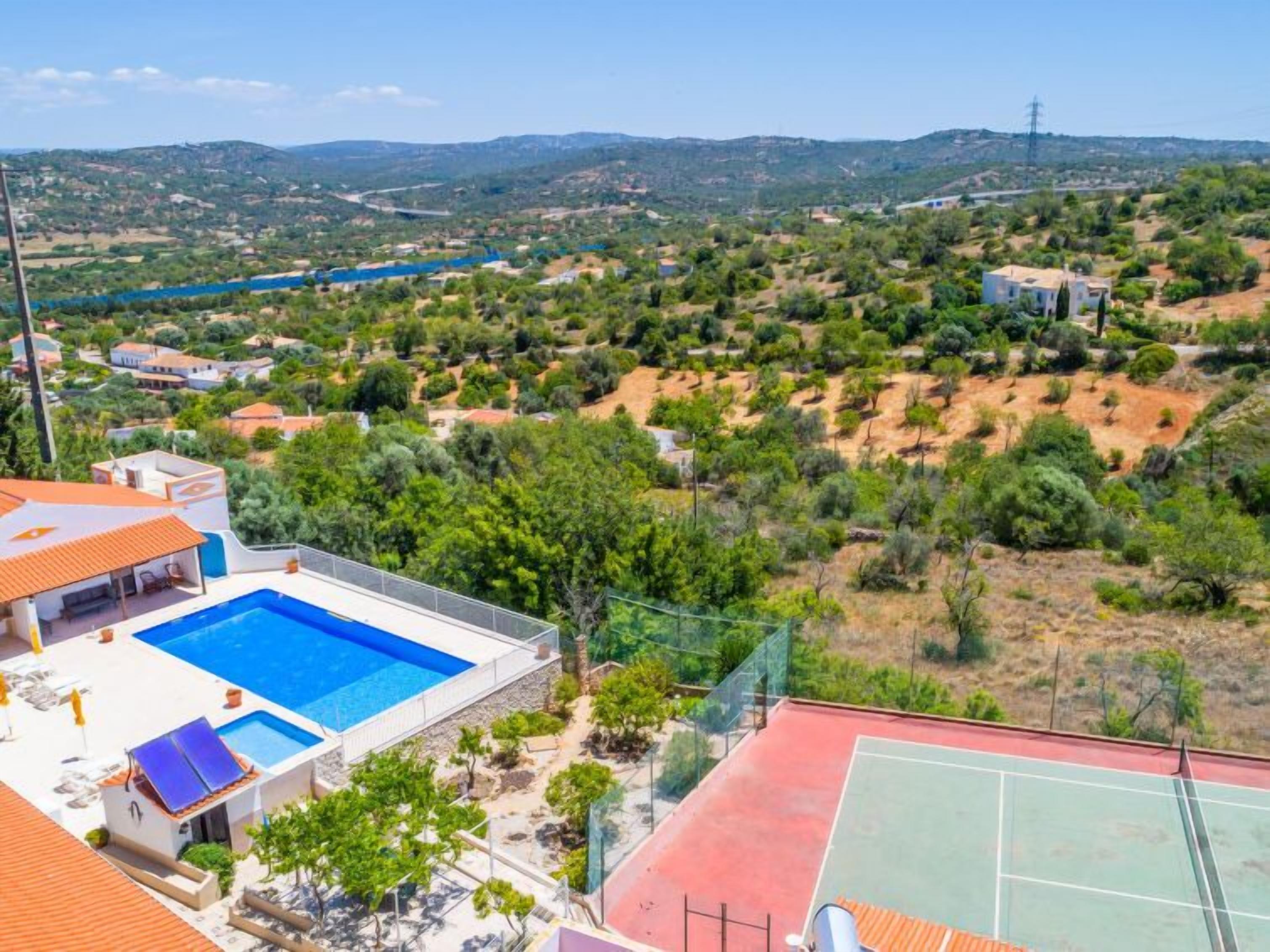 Une propriété résidentielle dotée d’une piscine, d’un court de tennis et offrant une vue sur un paysage vallonné.