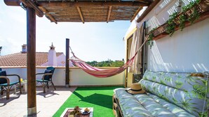 Una terraza en la azotea con una hamaca, un sofá y una mesa con comida y bebidas.