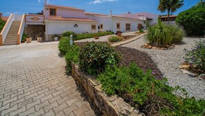 Un edificio de estilo mediterráneo tradicional con techo de tejas, una escalera de piedra y un patio empedrado con plantas y un camino de grava.