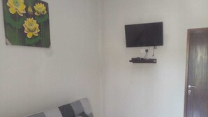 A living room with a sofa, a coffee table, a flat-screen TV mounted on the wall, and a door. - LEMBUNAI HOME STAY (Labuan Bajo)