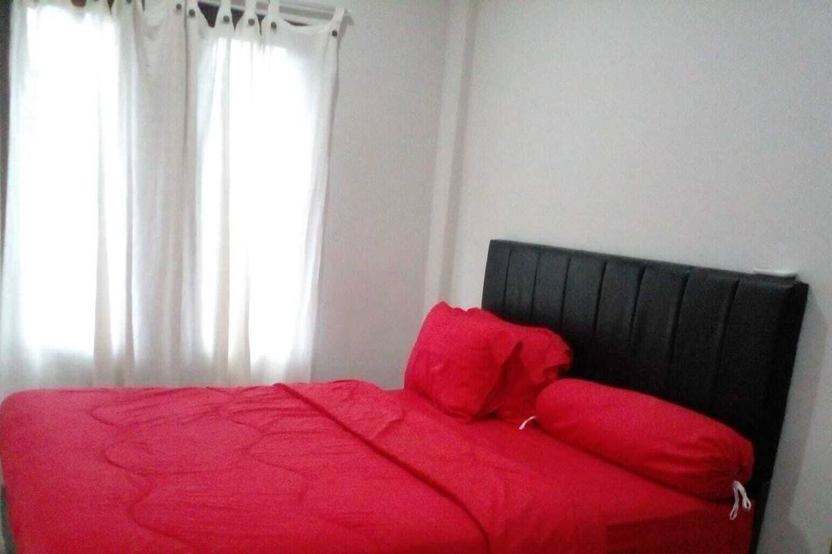 A bed with a black headboard and red bedding.