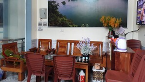 A dining area with wooden chairs and a table, a large scenic painting on the wall, and a small vase with flowers.