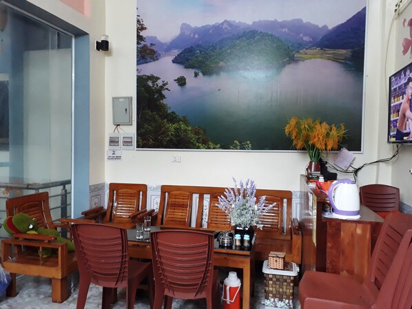 A dining area with wooden chairs and a table, a large scenic painting on the wall, and a small vase with flowers.