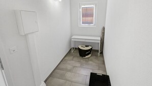 Une petite salle de bain propre, avec des toilettes blanches, un banc, une fenêtre donnant sur un paysage rayé et un interrupteur sur le mur.