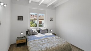 Une chambre avec un grand lit, deux tables de chevet, une fenêtre et une vue sur les bâtiments environnants.