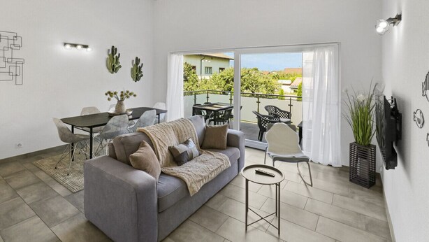 Un salon moderne avec un canapé gris, une table à manger et un balcon aménagé avec du mobilier d’extérieur.
