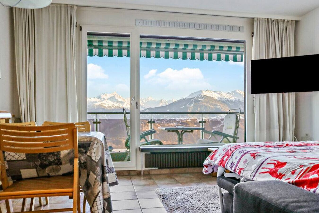 Une pièce comprenant un lit, une chaise, une table et offrant une vue sur les montagnes par une fenêtre.