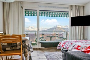Een kamer met een bed, een stoel, een tafel en uitzicht op bergen door een raam.