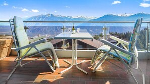 A balcony with two chairs and a table, overlooking a mountainous landscape.