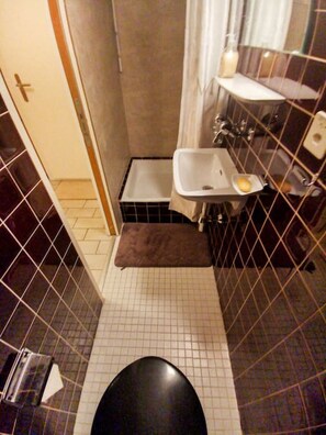 Un baño pequeño con azulejos, un inodoro, un lavamanos y una zona de ducha.