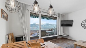 A dining area with a view of mountains, a television mounted on the wall, and a table with chairs.