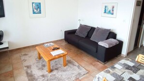 Una sala de estar con un sofá negro, una mesa de centro de madera y dos cuadros en la pared.