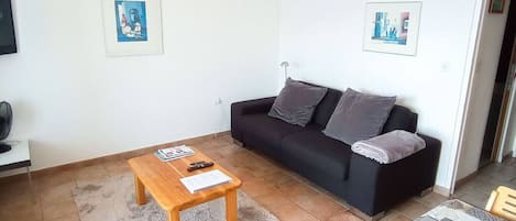 Una sala de estar con un sofá negro, una mesa de centro de madera y dos cuadros en la pared.