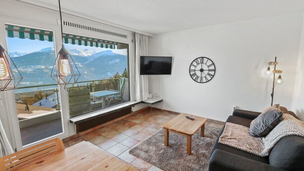 A living room with a large window, a flat-screen TV, a clock, and a sofa.