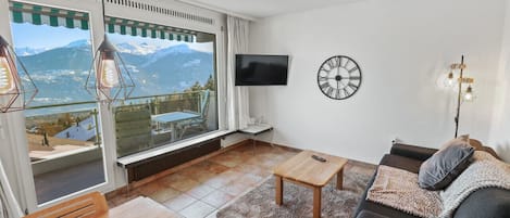 A living room with a large window, a flat-screen TV, a clock, and a sofa.