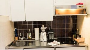 Cocina compacta con armarios blancos, salpicadero de azulejos negros, horno empotrado y un lavabo.