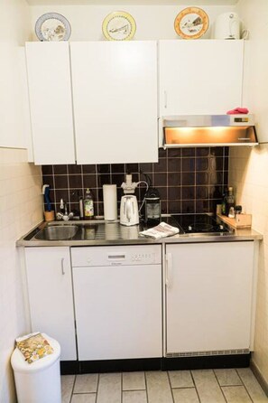 A compact kitchen with white cabinets, a black tiled backsplash, a built-in oven, and a sink. - Marigny 65 - Beautiful view, ideal for skiing, quiet location (Crans-Montana)