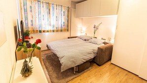 Une chambre à coucher avec un lit, un bureau, une télévision et une fenêtre avec des rideaux.