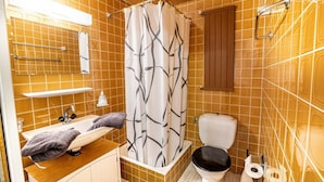 Une salle de bain avec un meuble-lavabo en bois, un lavabo blanc, des toilettes noires et un rideau de douche à motifs géométriques.