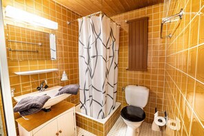 Une salle de bain avec un meuble-lavabo en bois, un lavabo blanc, des toilettes noires et un rideau de douche à motifs géométriques.