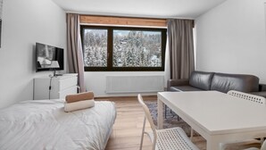 Una habitación de hotel moderna con cama, escritorio, silla, sofá, televisor y ventana con vista nevada.