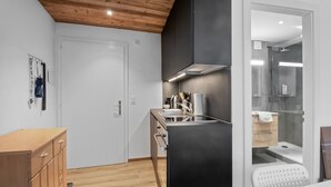 Cocina compacta con techo de madera, extractor de aire negro y zona de ducha con cerramiento de vidrio.