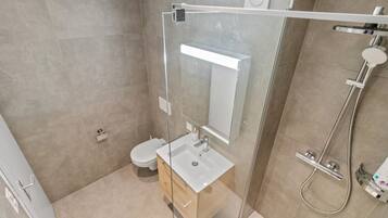 Ein modernes Badezimmer mit einer Duschkabine, einem weißen Waschbecken und einer Toilette.