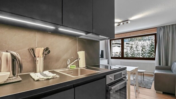Una cocina moderna con una isla grande, electrodomésticos de acero inoxidable y vistas a árboles nevados a través de una ventana.