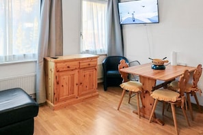 A room with a wooden dining table, chairs, a black office chair, a wooden cabinet, and a television on the wall.