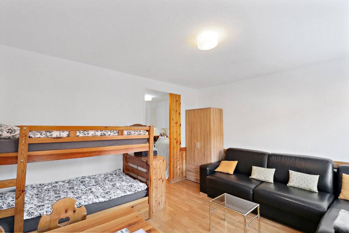Una habitació amb llits superposats, un sofà de pell negra, un armari de fusta i una taula petita.